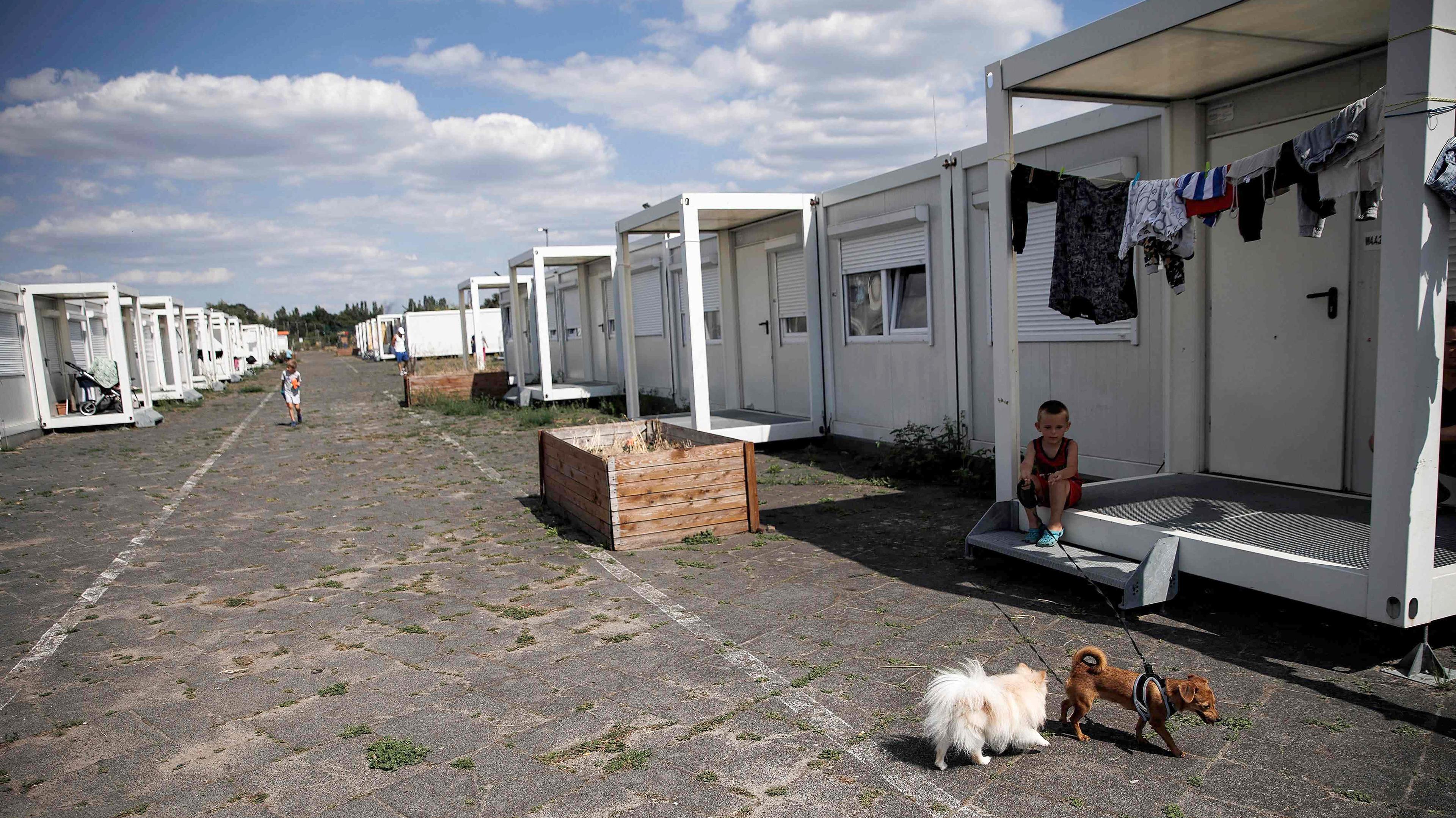 Ein Junge hält einen Hund an der Leine, während ein anderer an der Containerunterkunft für Flüchtlinge auf dem ehemaligen Flughafen Tempelhof in Berlin, Deutschland, vorbeiläuft, aufgenommen am 10.05.2023