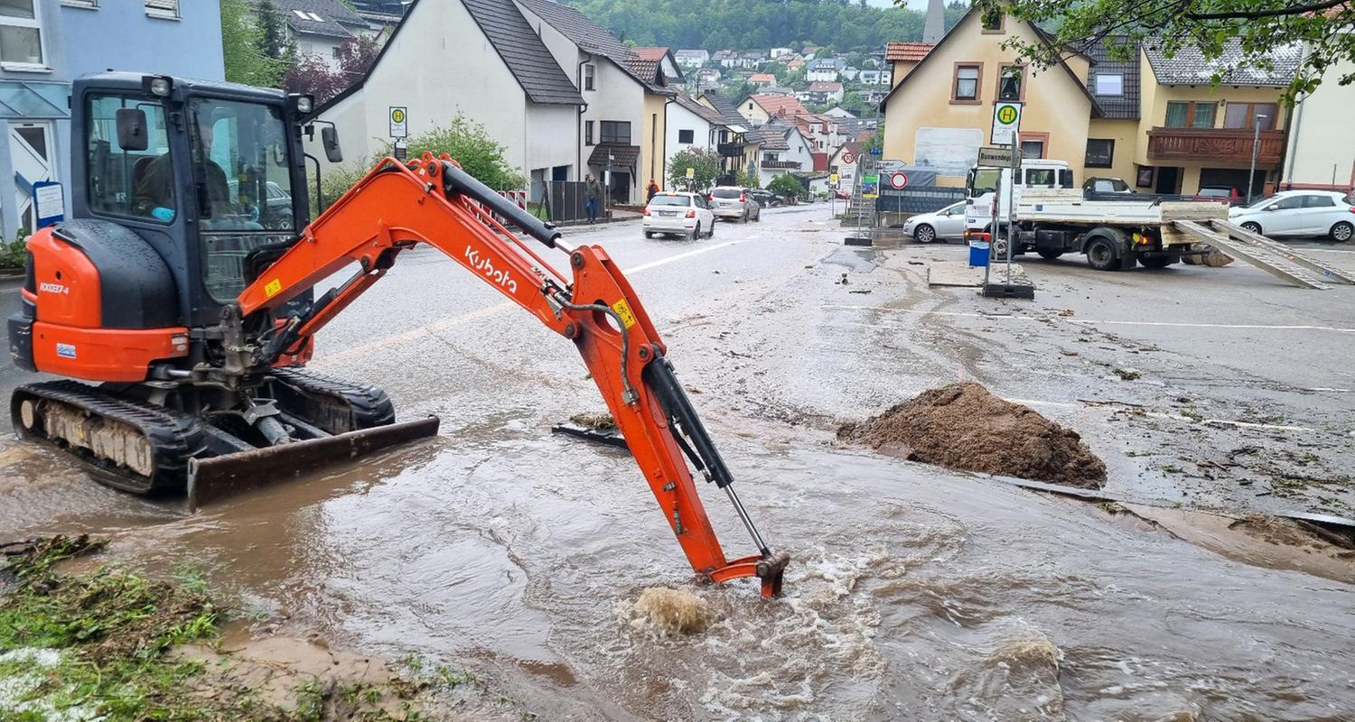 Baden-Württemberg, Schriesheim: Mit einem kleinen Bagger wird im Stadtteil Altenbach versucht den Bestbach frei zu schaufeln um das Wasser von der überfluteten Sraße abfließen zu lassen.