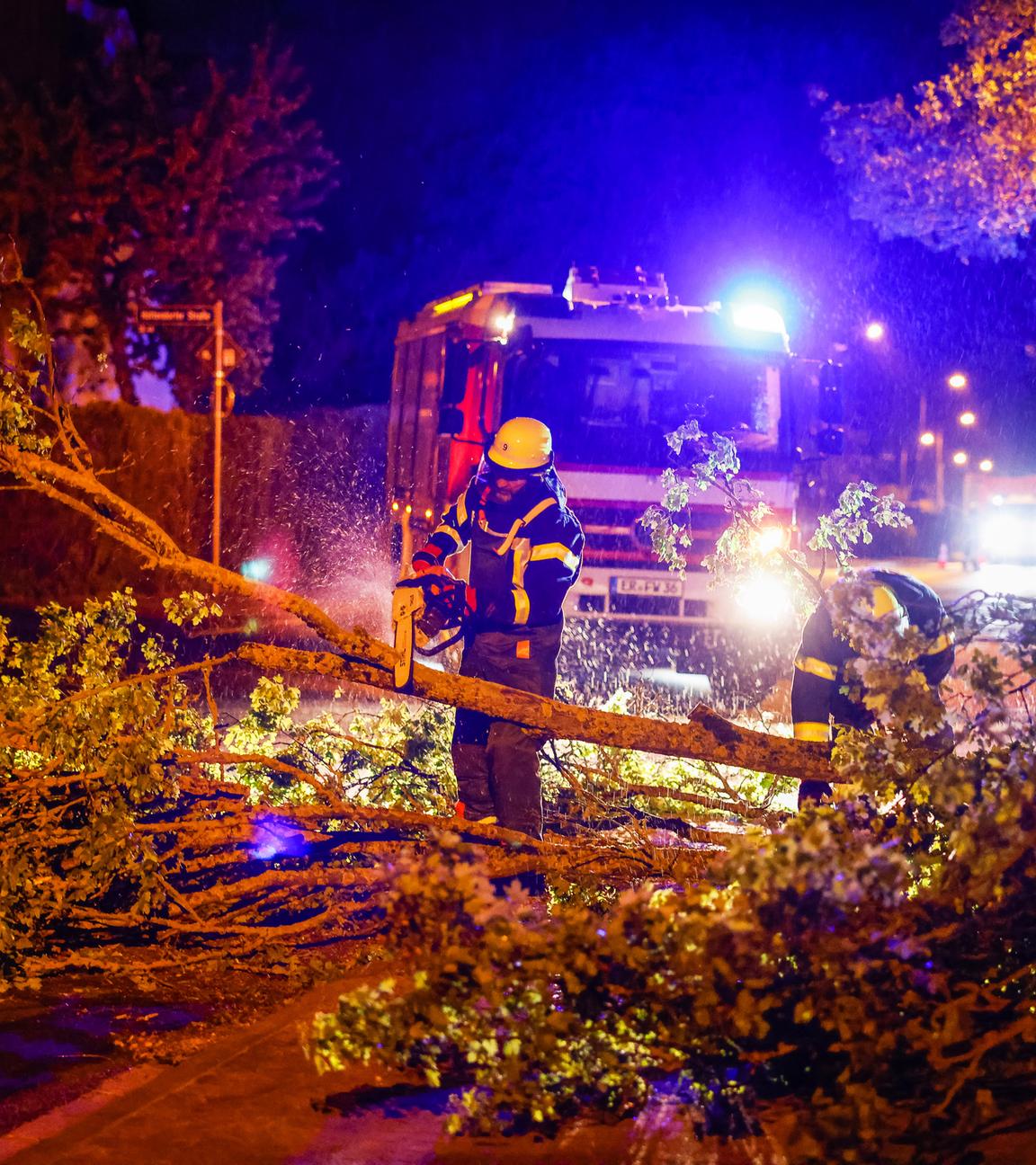 Einsatzkräfte der Feuerwehr zersägen mit einer Kettensäge einen umgestürzten Baum auf einer Straße im Regierungsbezirk Mittelfranken.