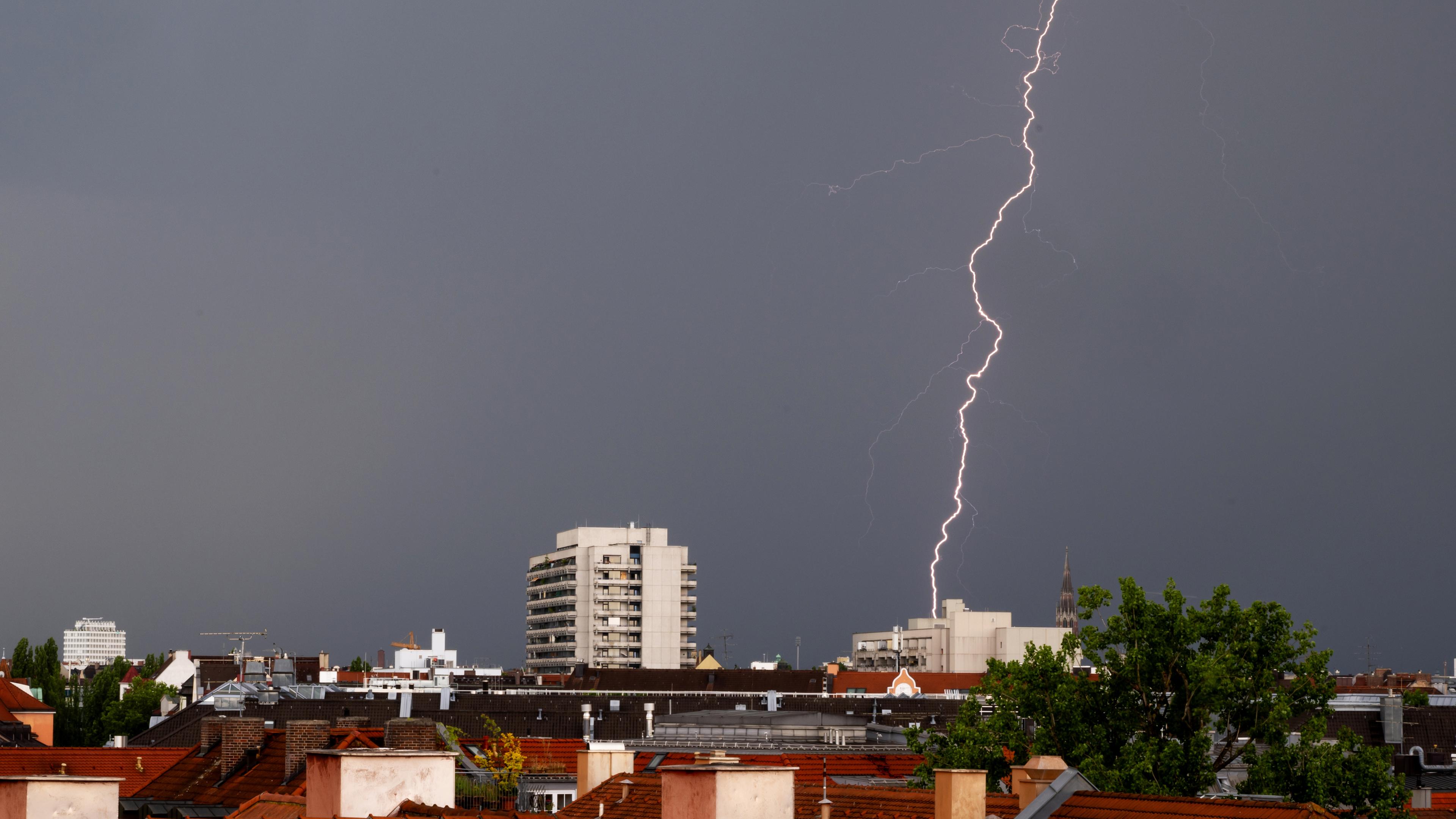 Bayern, München: Ein Gewitter mit Blitzen zieht in den Abendstunden über die Dächer der bayerischen Landeshauptstadt.