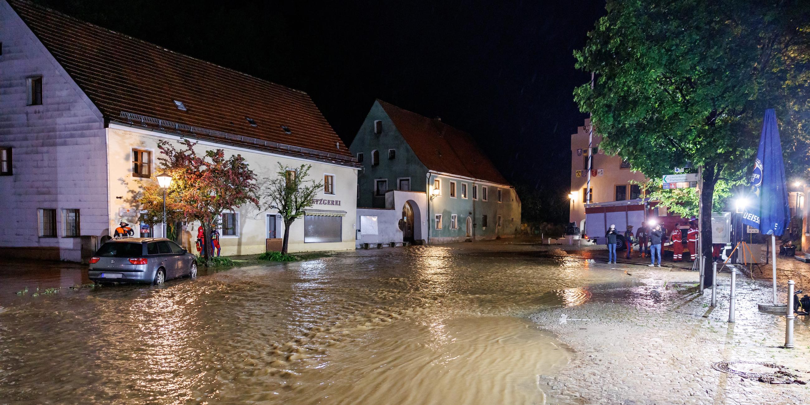 21.05.2024, Bayern, Kastl: Feuerwehrleute arbeiten in den Überflutungen. Wassermassen fließen nach starkem Regen aus dem Fluss Lauterach über den Marktplatz in der Gemeinde Kastl.