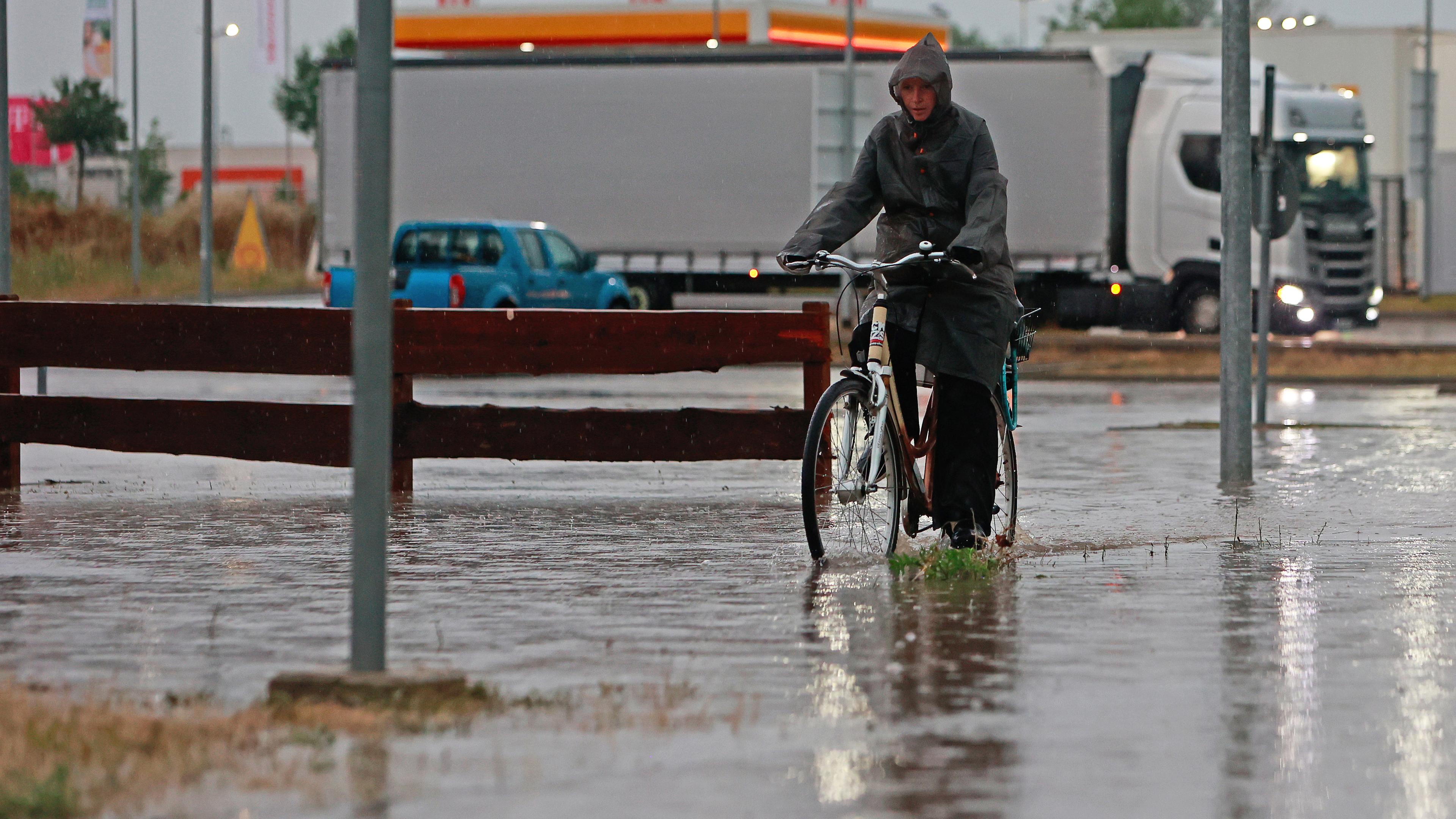 Eine Frau fährt nach einem Unwetter mit Starkregen mit ihrem Fahrrad über eine überflutete Straße in einem Gewerbegebiet
