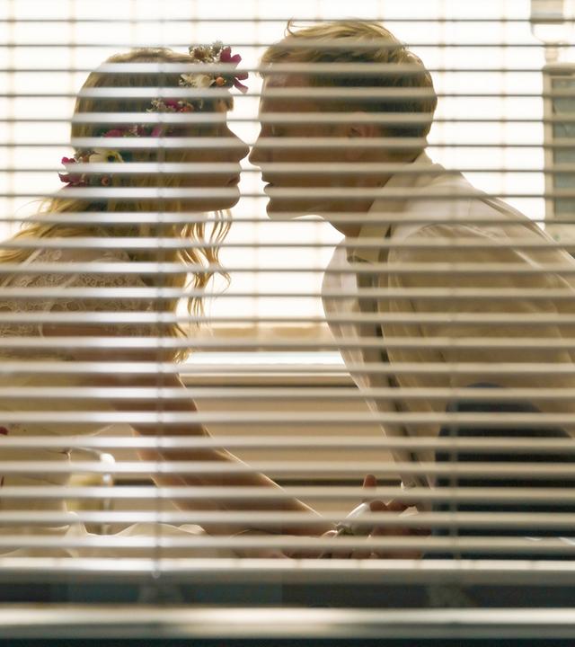 Vivian (Anna Hausburg) und Freddy (Anton Spieker) wollen heiraten. Das Paar nähert sich auf einem Krankenbett sitzend zum Kuss an.