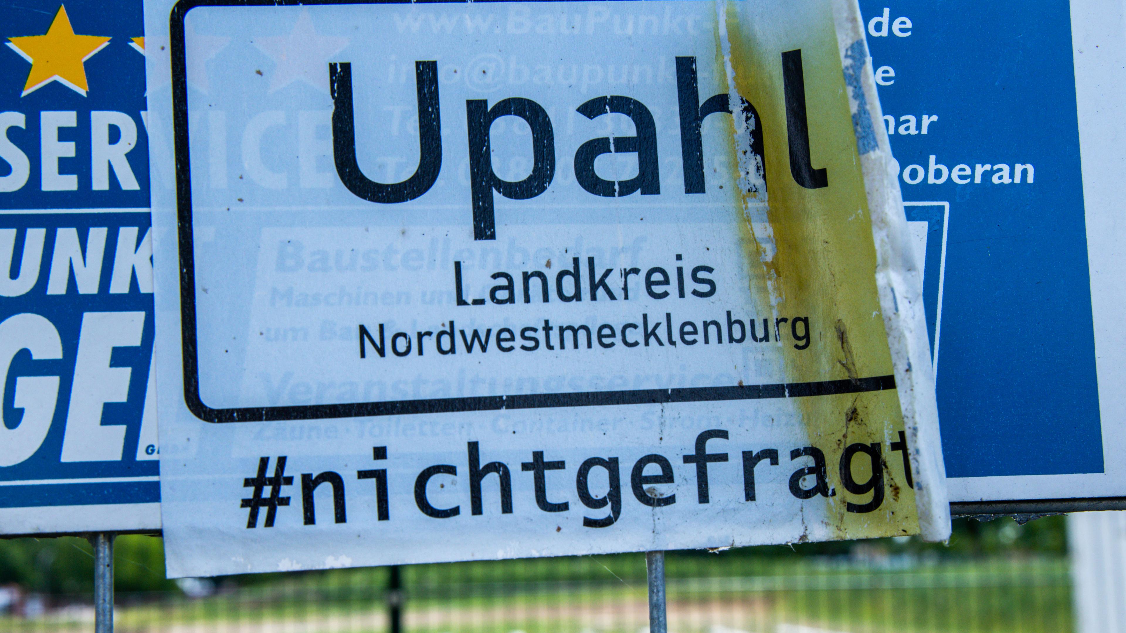 Mecklenburg-Vorpommern, Upahl: Ein Protestschild hängt am Bauzaun vor der stillstehenden Baustelle für eine geplante Flüchtlingsunterkunft im Gewerbegebiet. 