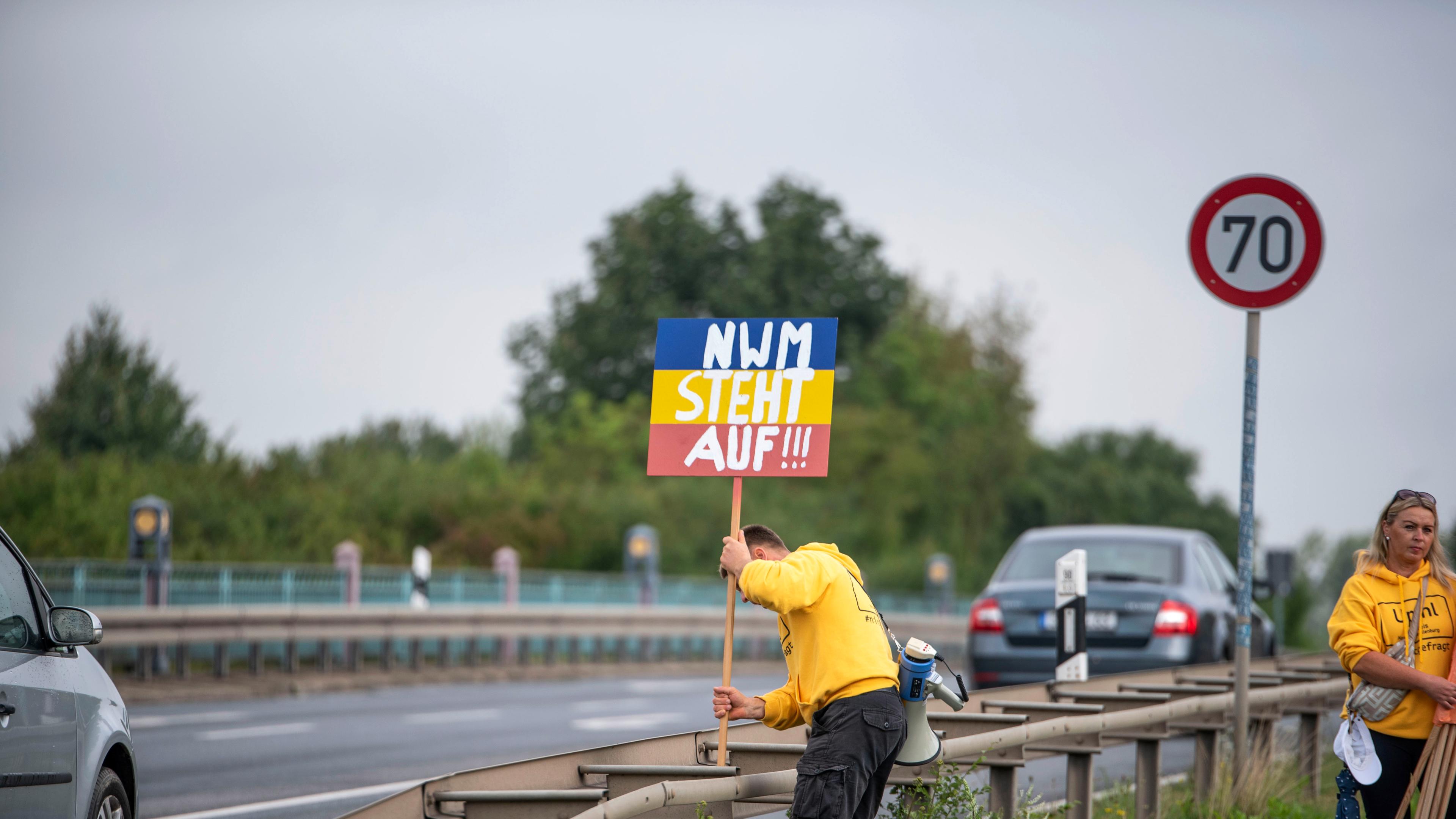 Mecklenburg-Vorpommern, Upahl: Ein Mann steckt an der Hauptstraße ein Schild mit der Aufschrift "NWM steht auf!!!" an eine Leitplanke als Protest gegen den Bau einer Flüchtlingsunterkunft in Upahl im Landkreis Nordwestmecklenburg (NWM).