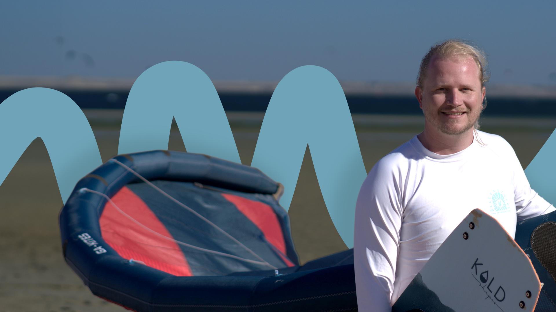 Patrick Bauer steht mit Kite und Board am Strand 