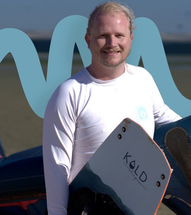 Patrick Bauer steht mit Kite und Board am Strand 