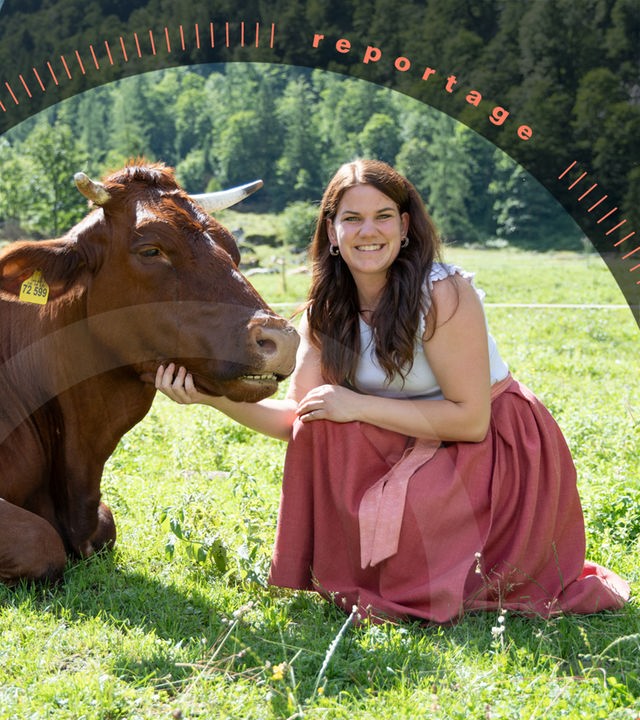 Veronika hockt neben einer liegenden Kuh auf einer Weide und schaut lächelnd in die Kamera.