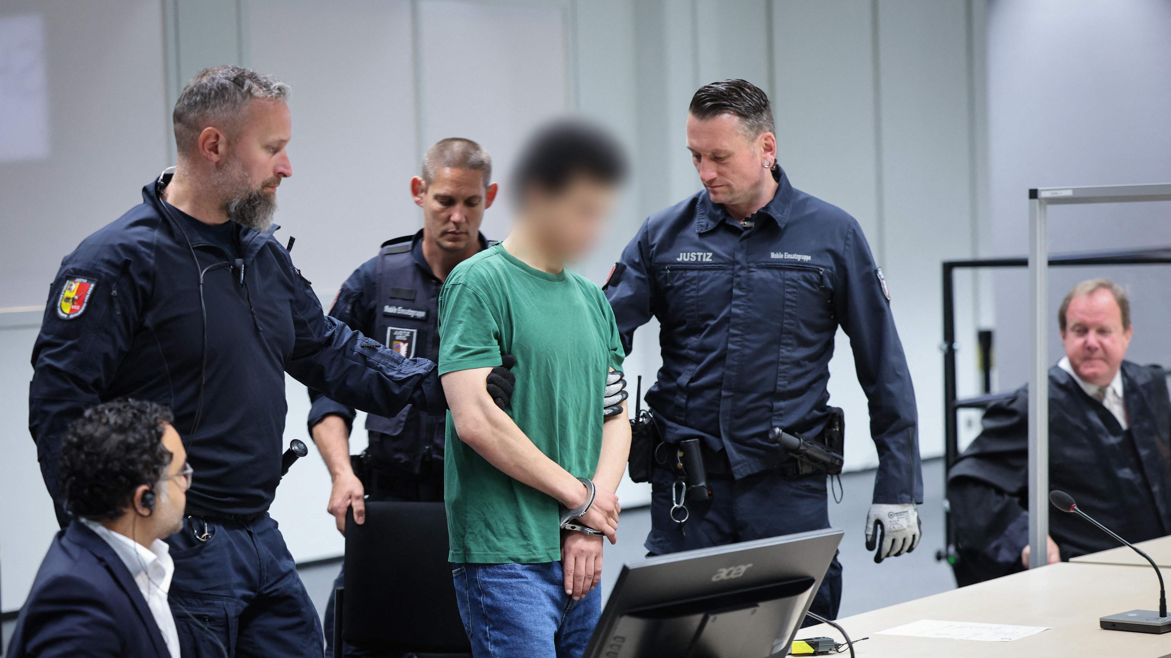 Der Angeklagte Ibrahim A. (4. L.) wird am 15. Mai 2024 von Justizbeamten im norddeutschen Itzehoe in Handschellen und Fußfesseln in den Gerichtssaal des China Logistic Center gebracht.