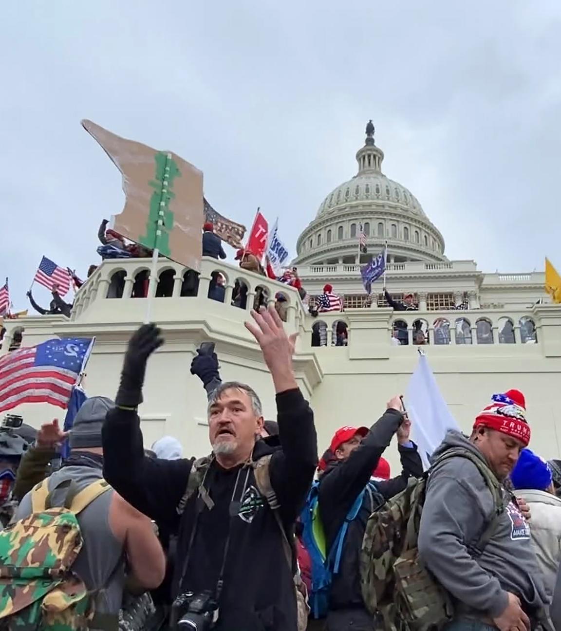 Demonstrierende Menschen stehen vor einer weißen Mauer unter einer Brüstung am Fuße des Kapitols der Vereinigten Staaten, eines Kuppelbaus.