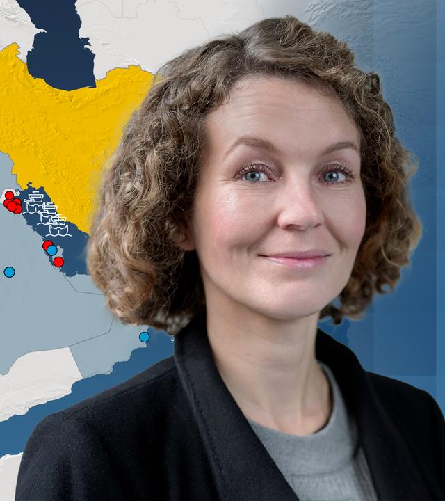Die Nahost-Analystin Marie-Theres Sommerfeld vom GIDS im Vordergrund, im Hintergrund eine Karte des Iran mit seinen Atomprogrammen und eingezeichnete Flugzeugträger und Kampfschiffe der USA.