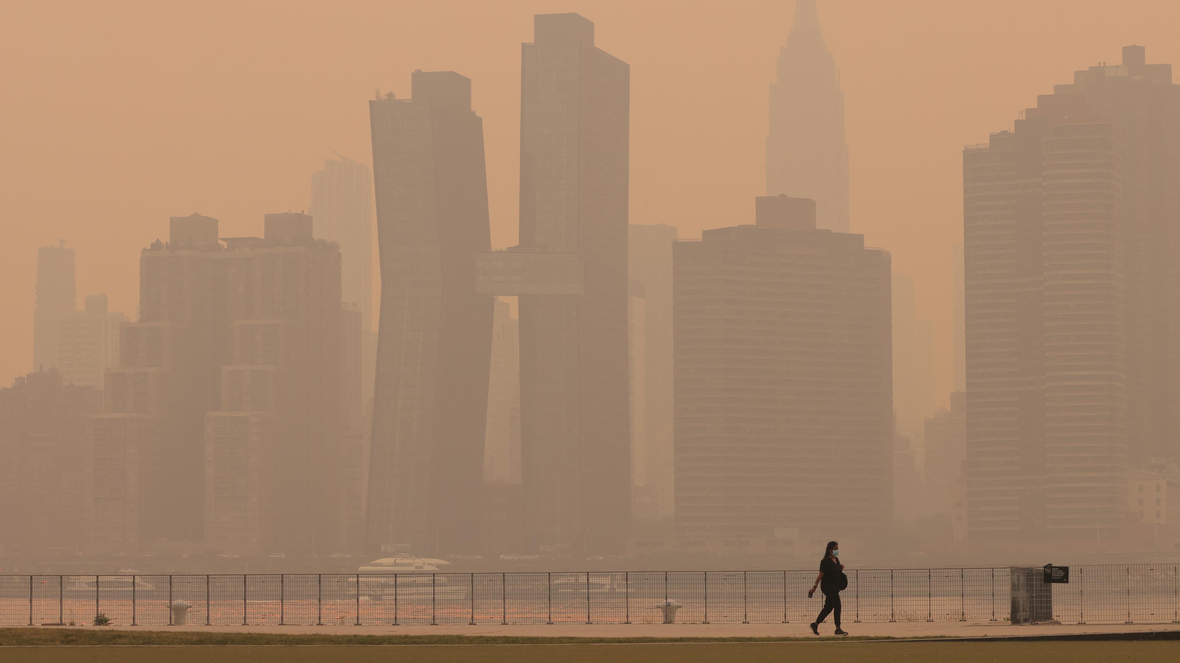 USA, New York: Eine Frau geht am Ufer des East River entlang. Rauch der kanadischen Waldbrände hängt über Manhattan.