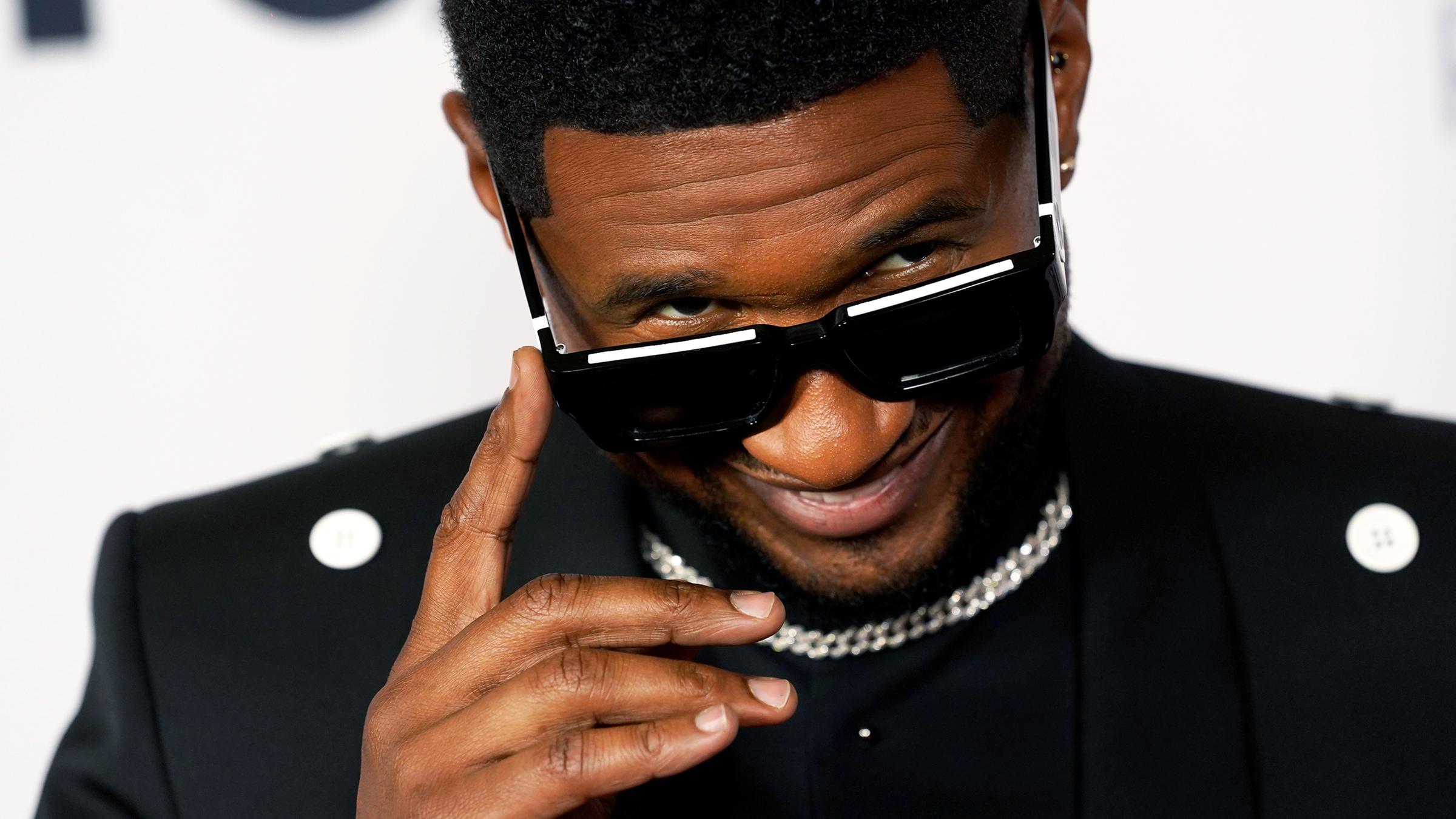Usher blickt über die Ränder seiner Brille an der Kamera vorbei