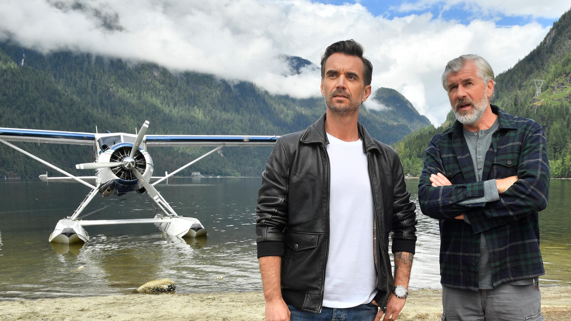 Max Parger (Florian Silbereisen) und Martin Grimm (Daniel Morgenroth) stehen am Ufer eines Sees nebeneinander. Martin hat die Arme vor der Brust verschränkt und redet mit Max. Im Hintergrund steht ein Wasserflugzeug.