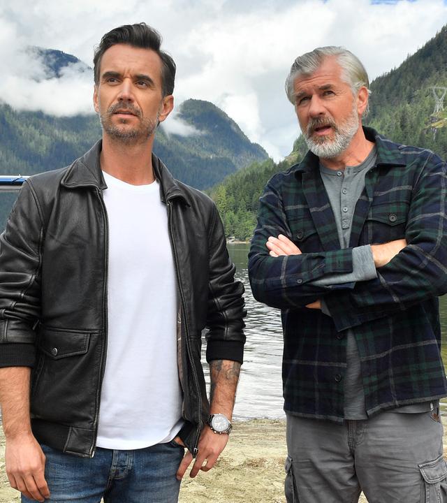 Max Parger (Florian Silbereisen) und Martin Grimm (Daniel Morgenroth) stehen am Ufer eines Sees nebeneinander. Martin hat die Arme vor der Brust verschränkt und redet mit Max. Im Hintergrund steht ein Wasserflugzeug.