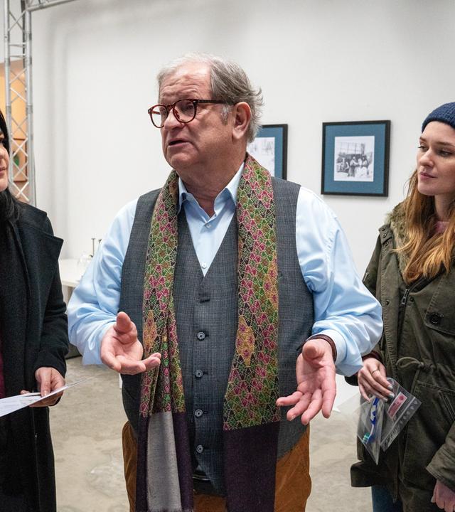 "Letzte Spur Berlin - Vatergefühle": Mina Amiri (Jasmin Tabatabai) und Lucy Elbe (Josephin Busch) stehen im Raum einer Kunstausstellung bei dem Kunsthändler Gregor Witte (Anton Rattinger). Witte gestikuliert mit seinen Händen. Mina und Lucy sehen ihn an. Mina hält ein Blatt Papier in ihren Händen.