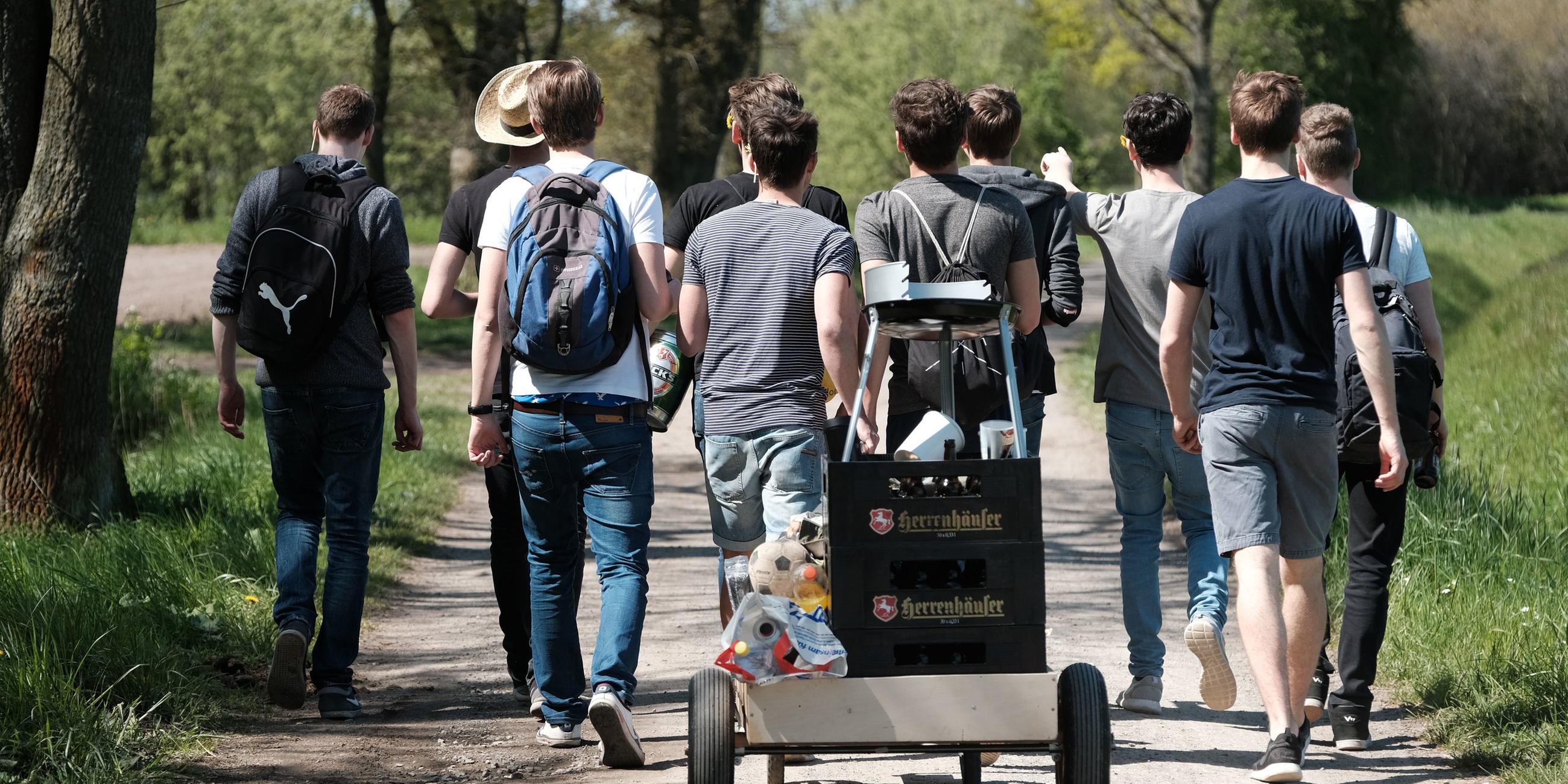 Eine Gruppe junger Männer von hinten auf einer Vatertags-Wanderung mit Bollerwagen.