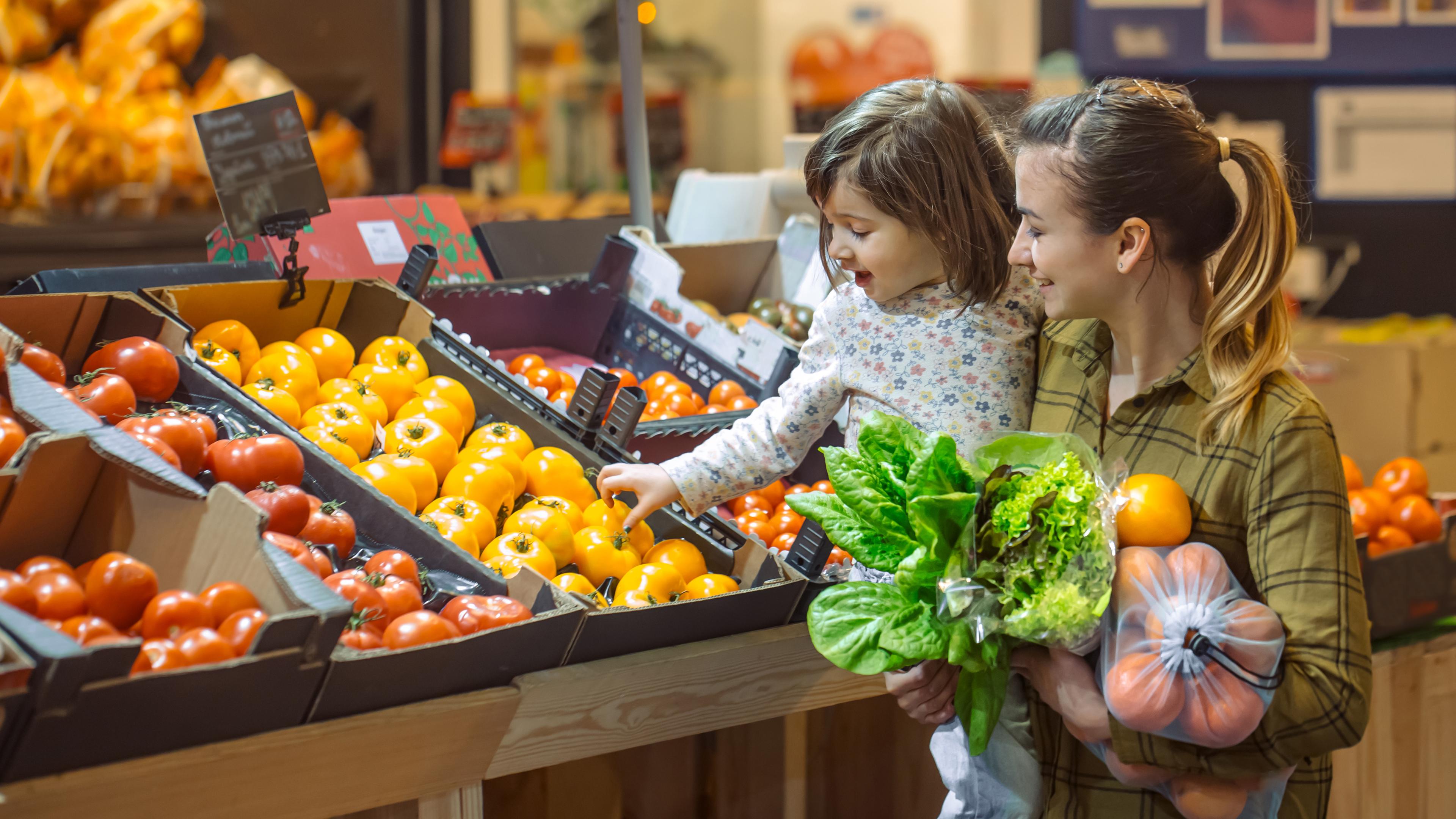 Frau mit Kind auf dem Arm kauft Obst im Supermarkt.