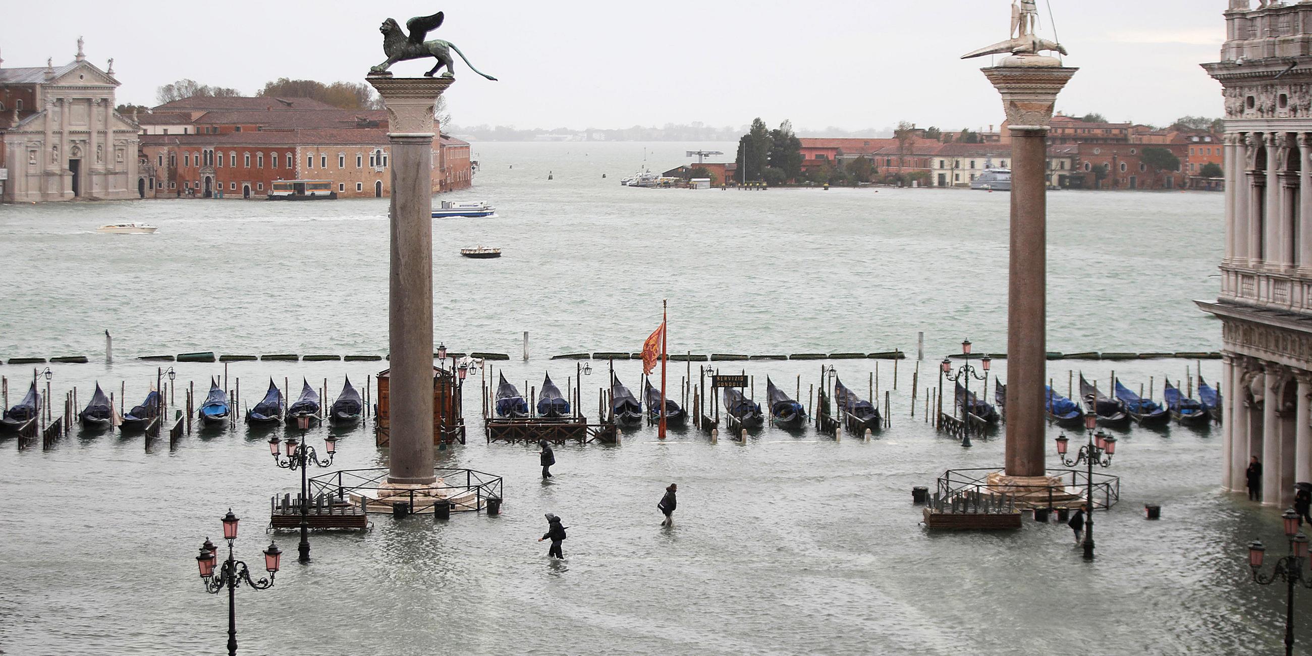 Menschen gehen knietief im Wasser über den überfluteten Markusplatz. Am 15.11.2019 in Venedig, Italien.