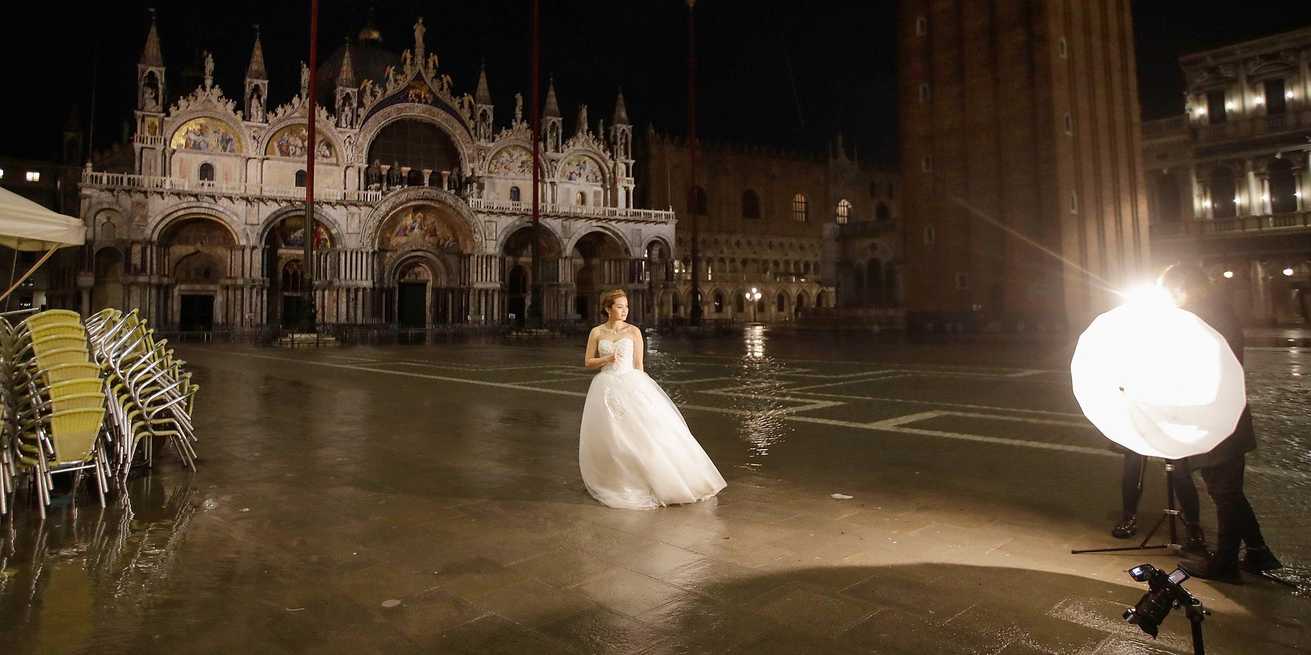 Eine Frau im Brautkleid steht am frühen Morgen auf dem überfluteten Markusplatz und wird fotografiert. Am 15.11.2019 in Venedig, Italien.