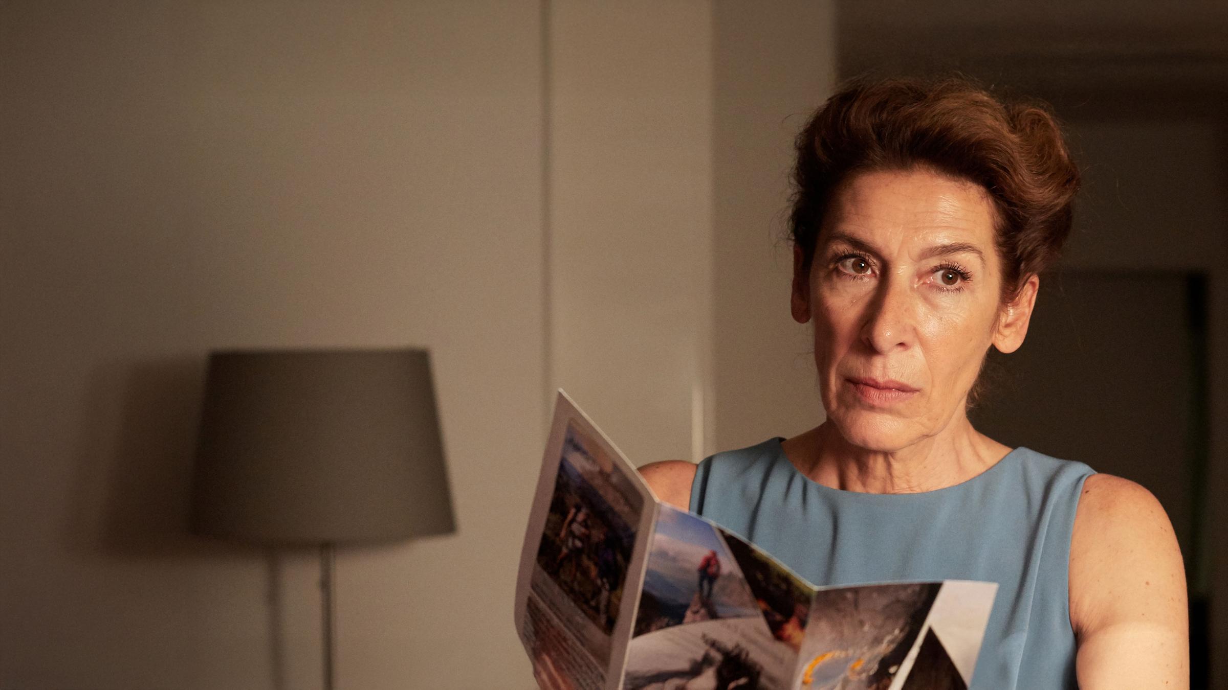 Gitti Kronlechner (Adele Neuhauser) liest in einem Prospekt und schaut nachdenklich.