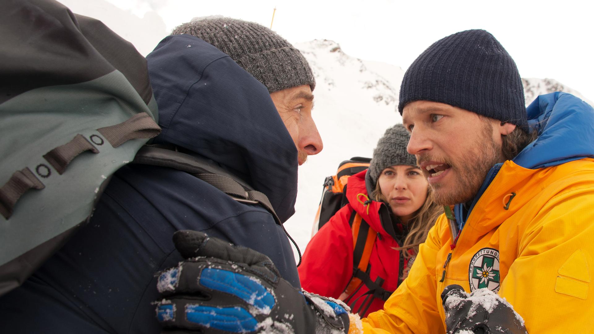 Die Bergretter Markus (Sebastian Ströbel, r.) und Katharina (Luise Bähr, M.) versuchen, den aufgebrachten Chris Haffner (Gabriel Raab, l.) zu beruhigen.