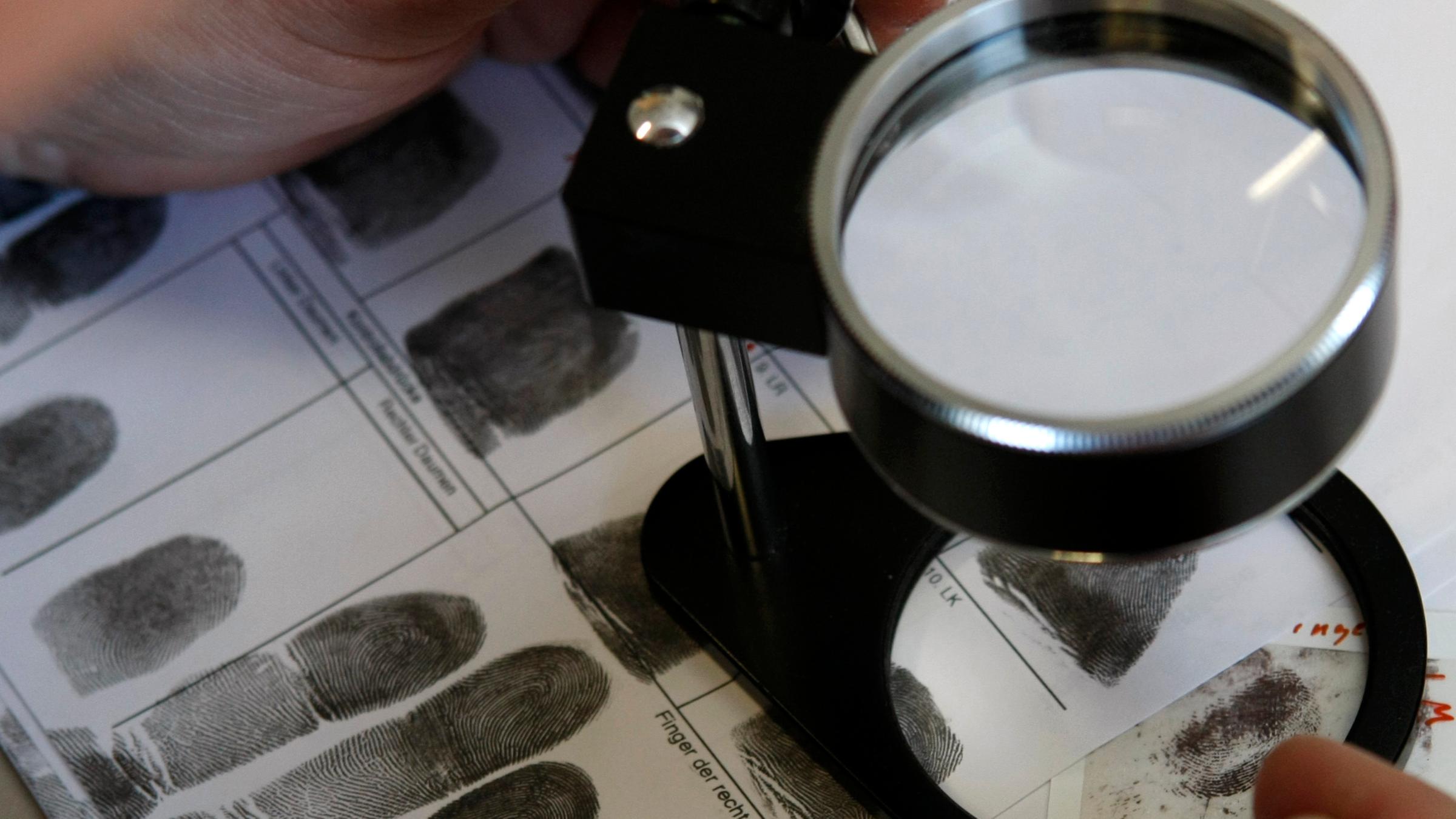 "Verbrechen auf der Spur": Ein Kriminaltechniker vergleicht Fingerabdrücke unter einer Lupe.