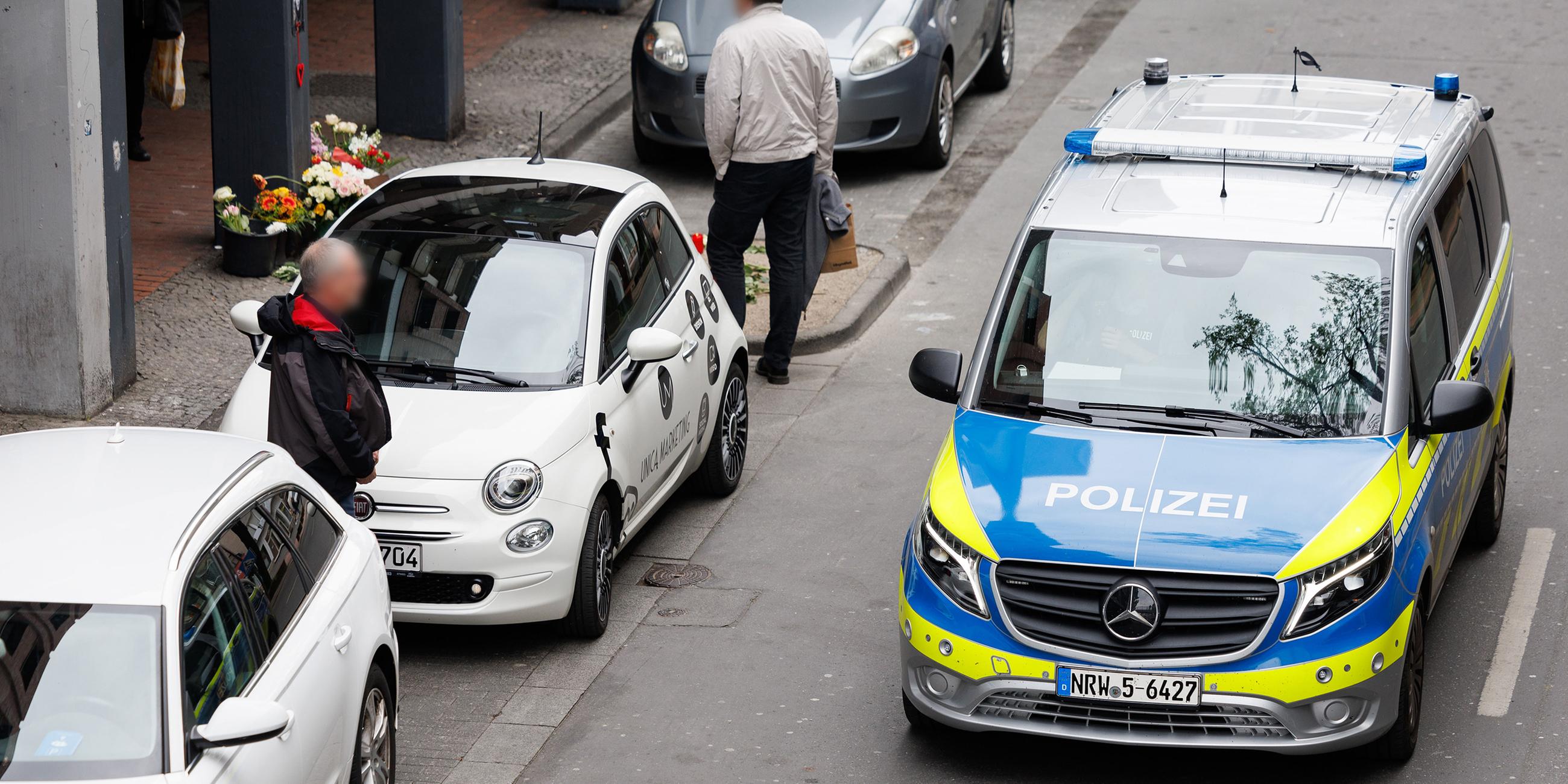 Trauerkerzen stehen an einem Tatort in der Paderborner Innenstadt, an dem die Polizei mit einem Fahrzeug entlang fährt.
