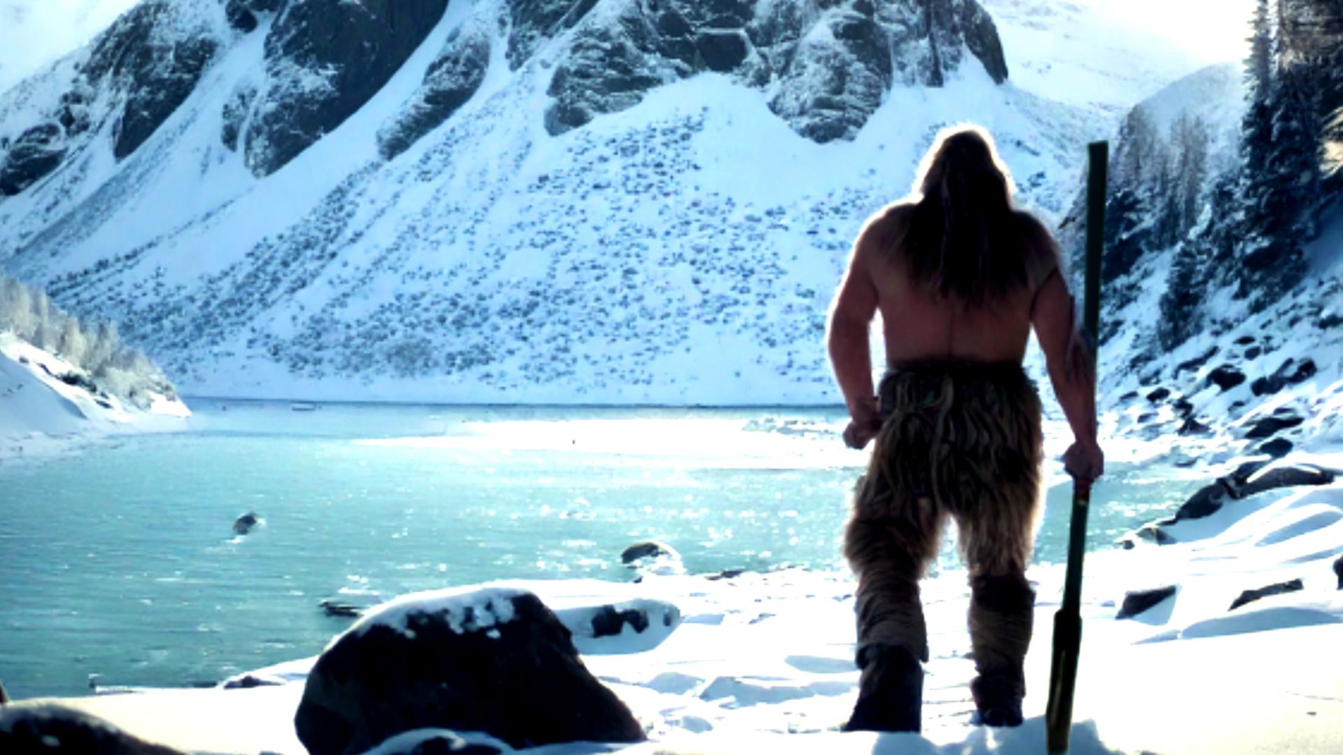 Ein Steinzeitmensch blickt auf eine bergige Winterlandschaft. Im Hintergrund ist der Himmel grün eingefärbt.