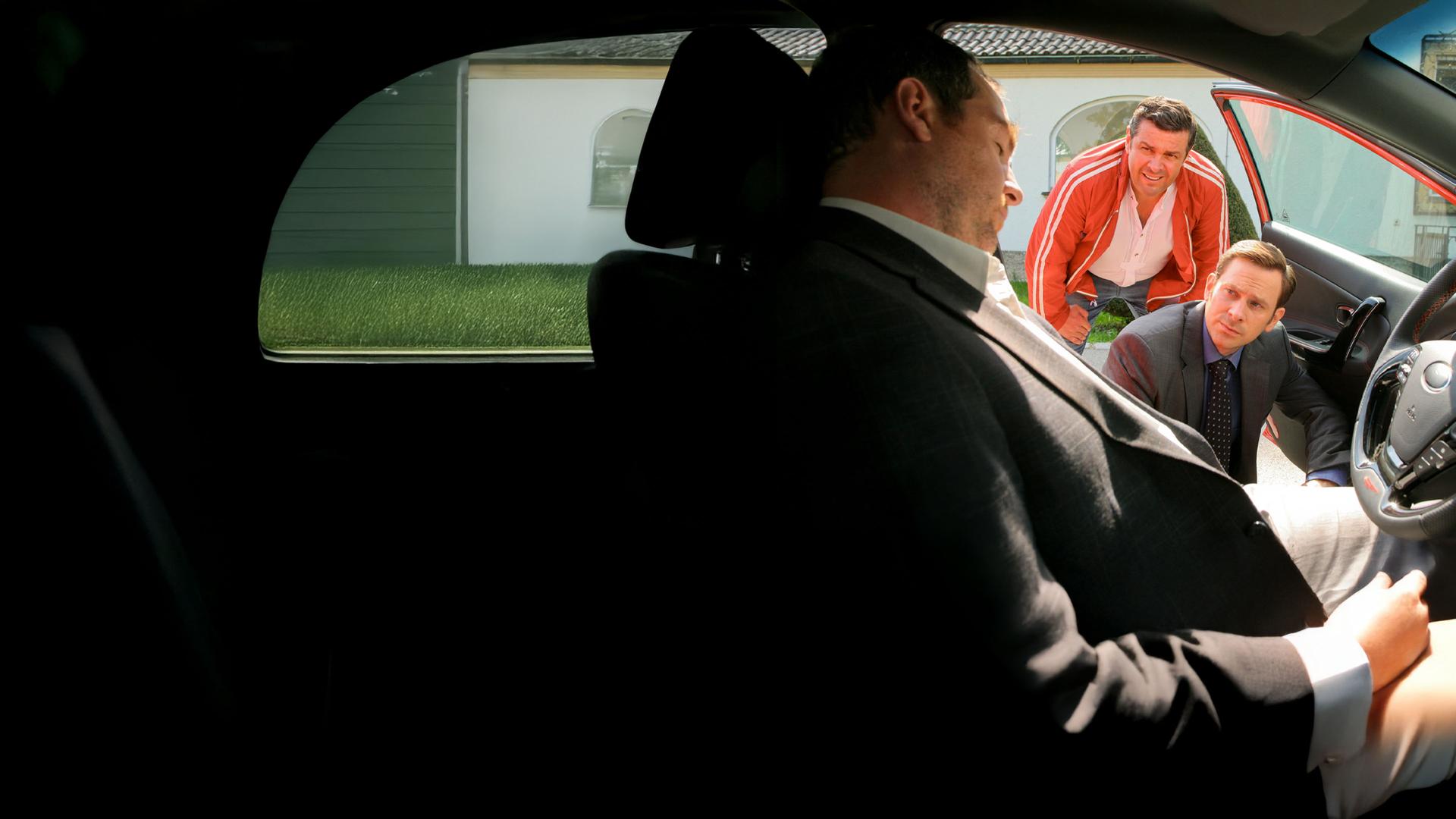 "Die Rosenheim-Cops - Vergeigtes Leben": Vor der Musikakademie stehen Kommissar König (Mark-Alexander Solf) und Times-Square-Wirt Jo (Christian K. Schaeffer) an der geöffneten Tür eines Autos, in dem sie die Leiche von Musiker Edward Kellenberger auffinden.