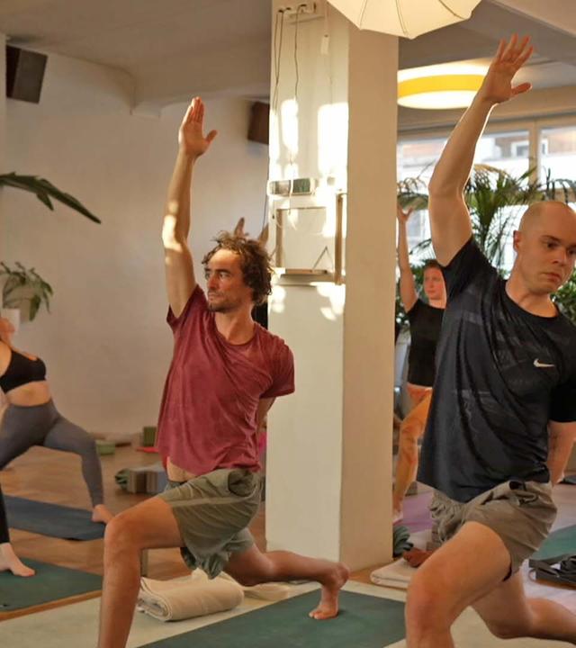 Gruppe an Personen in einem Studio, die Yoga betreiben.