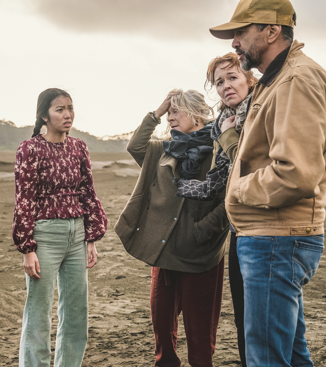 Im sandigen Gelände stehen Issie, Caleb und Caroline gegenüber von Mitch, Amanda und Tom. Alle schauen besorgt. Der Himmel ist grau.