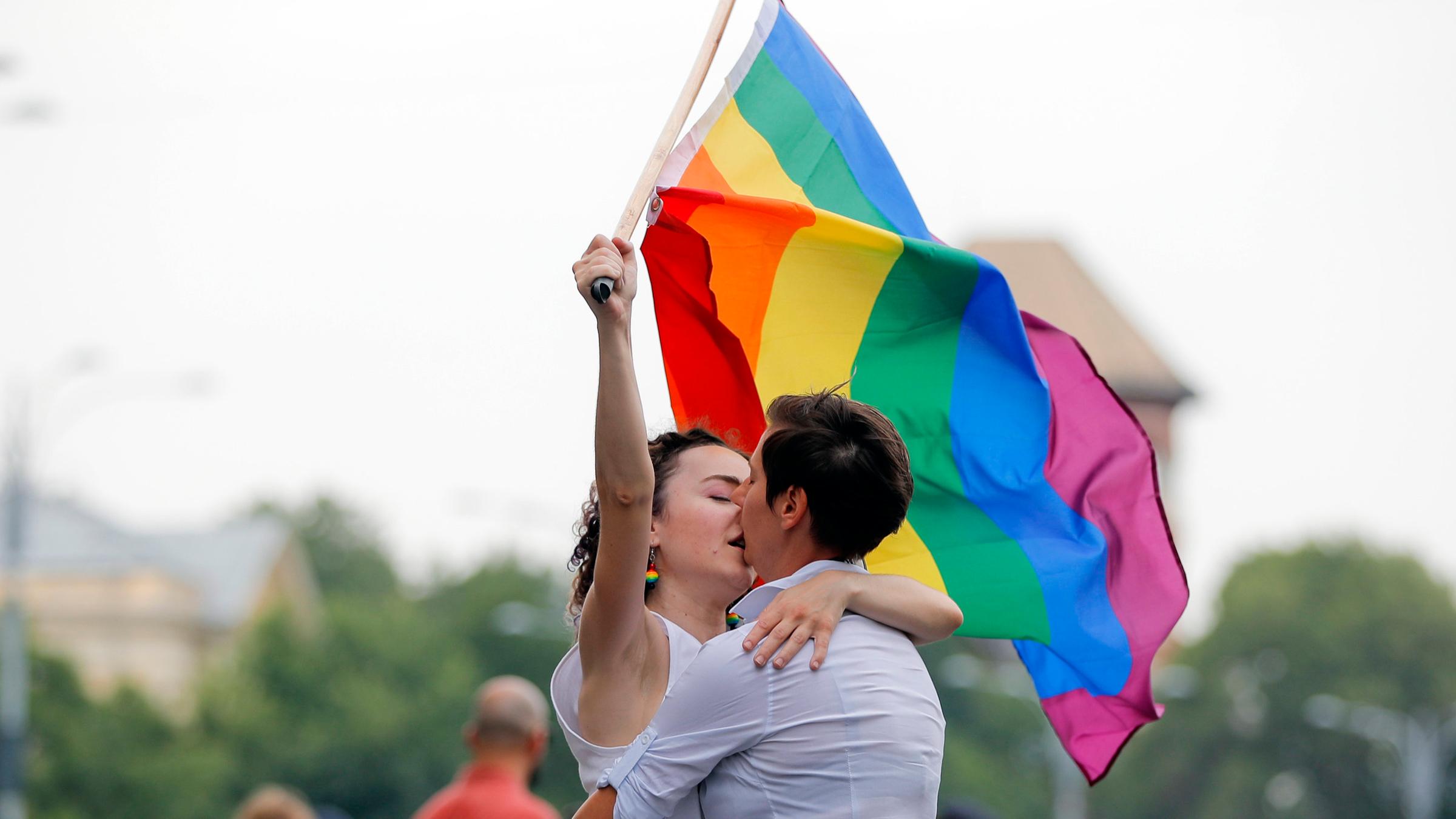  Zwei Frauen küssen sich, eine von ihnen hält eine Regenbogenflagge in der Hand.