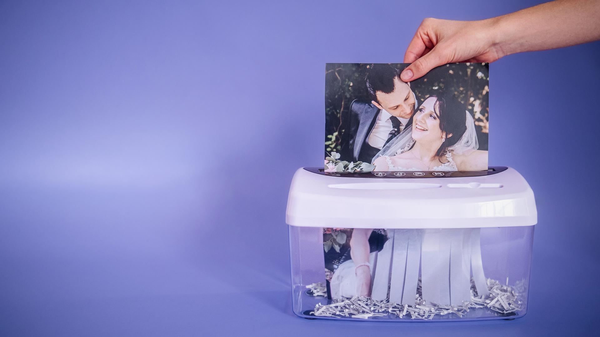 Ein Hochzeitsfoto mit Jessica und Sebastian wird von einer Hand in den Papierschredder gesteckt.