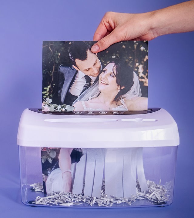 Ein Hochzeitsfoto mit Jessica und Sebastian wird von einer Hand in den Papierschredder gesteckt.