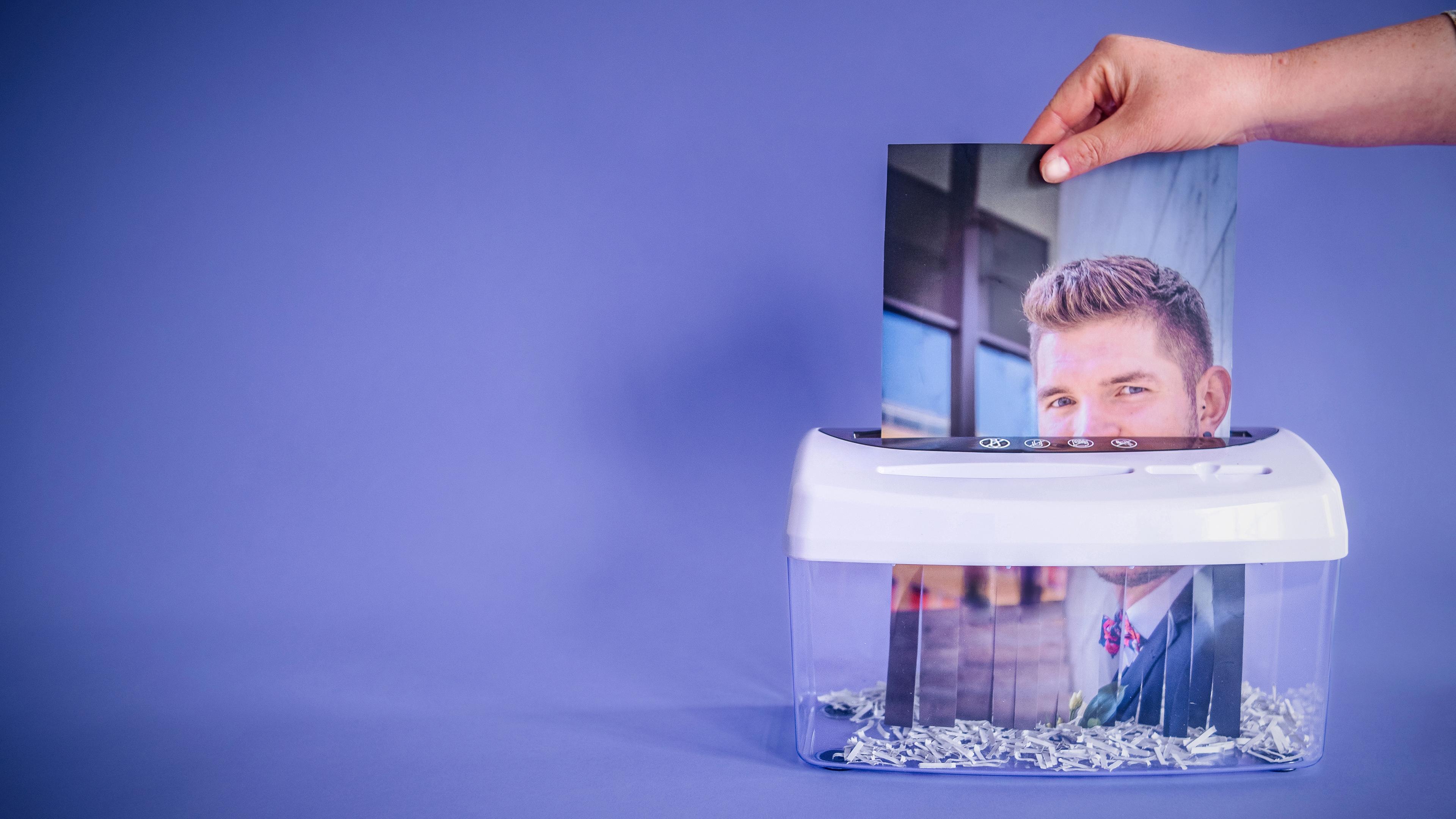 Foto mit Patrick wird von einer Hand in den Papierschredder gesteckt.