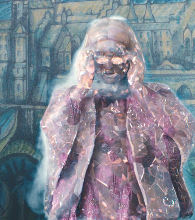 In der Aula: Entsetzt blickt Mildred zu der neben ihr stehenden Frau Graustein. Die fasst sich mit beiden Händen an die Brillenbügel, und ihr ganzer Körper verwandelt sich zu Glas, das bereits mit Rissen durchzogen ist.