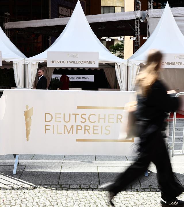 Eine Frau geht am Schriftzug "Deutscher Filmpreis" centlang vor der 75. Verleihung des Deutschen Filmpreises in Berlin vorbei.