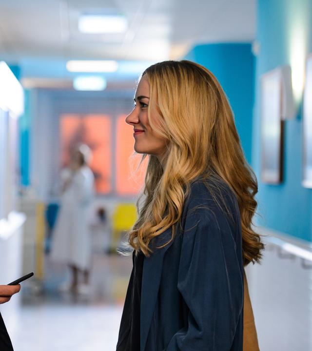 "Bettys Diagnose - Verlust": Dr. Frank Stern (Max Alberti) und Betty Weiss (Annina Hellenthal) begegnen sich nach Feierabend auf dem Flur der Klinik und lächeln einander an.