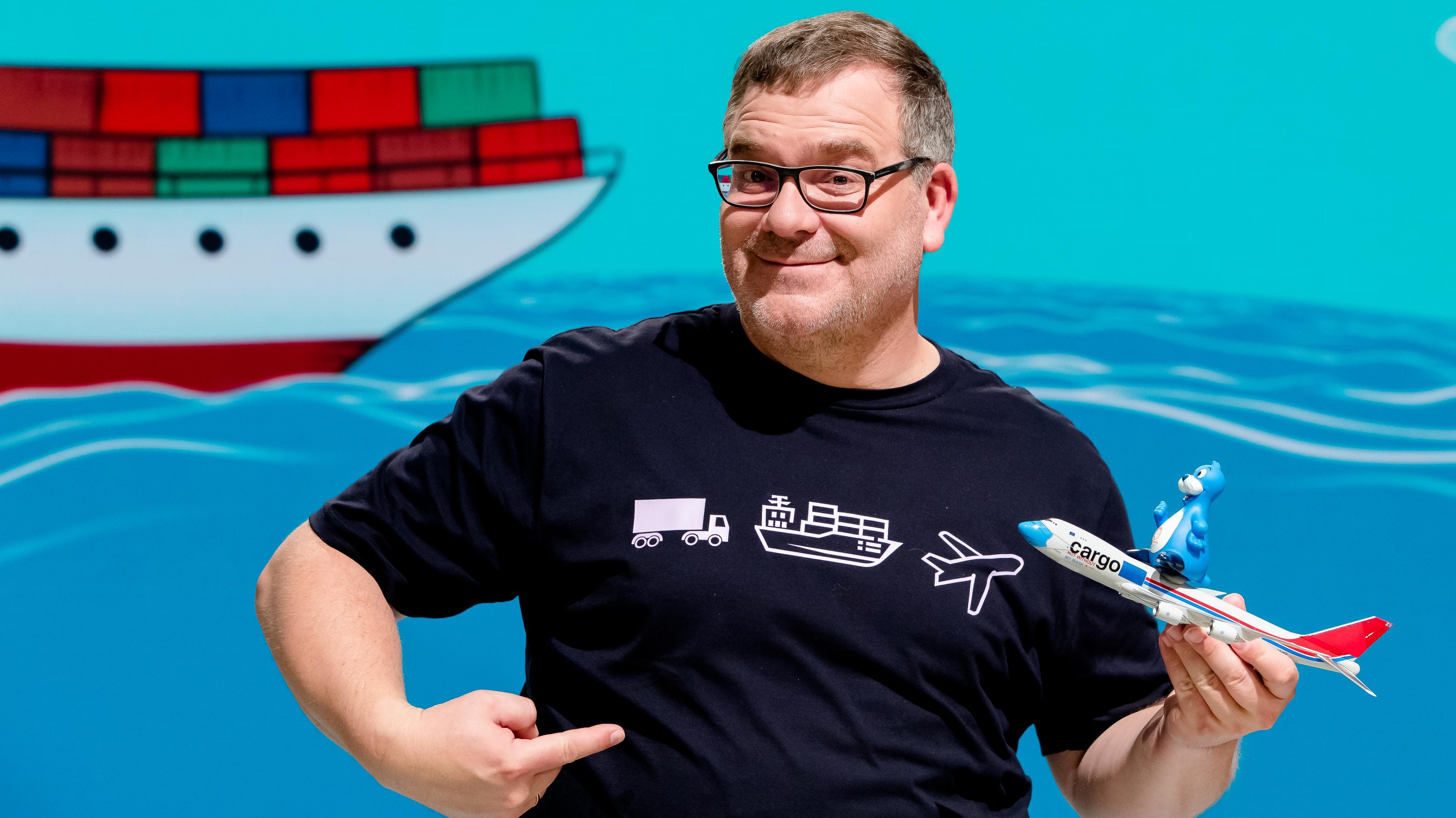 1, 2 oder 3: Moderator Elton steht vor der Vidiwall im "1, 2 oder 3"-Studio. Er hält ein Modellflugzeug in der Hand.