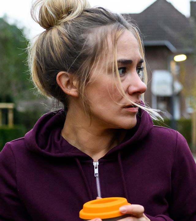 Betty (Annina Hellenthal) steht mit einem Kaffeebecher auf dem Parkplatz vor der Klinik. Sie schaut verängstigt und angespannt über ihre Schulter. Rike Köhler (Isabell Horn) steht hinter ihr, ihr Fahrrad liegt auf dem Boden.