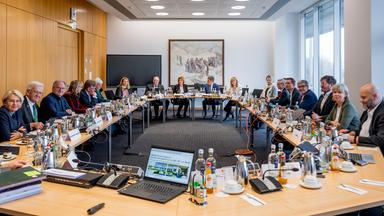 Weitwinkelaufnahme: ZDF-Verwaltungsratssitzung in einem Konferenzraum mit U-förmig angeordneten Tischen und zahlreichen Teilnehmenden. Die Sitzung steht unter dem Vorsitz von Malu Dreyer, auch ZDF-Intendant Norbert Himmler ist anwesend.