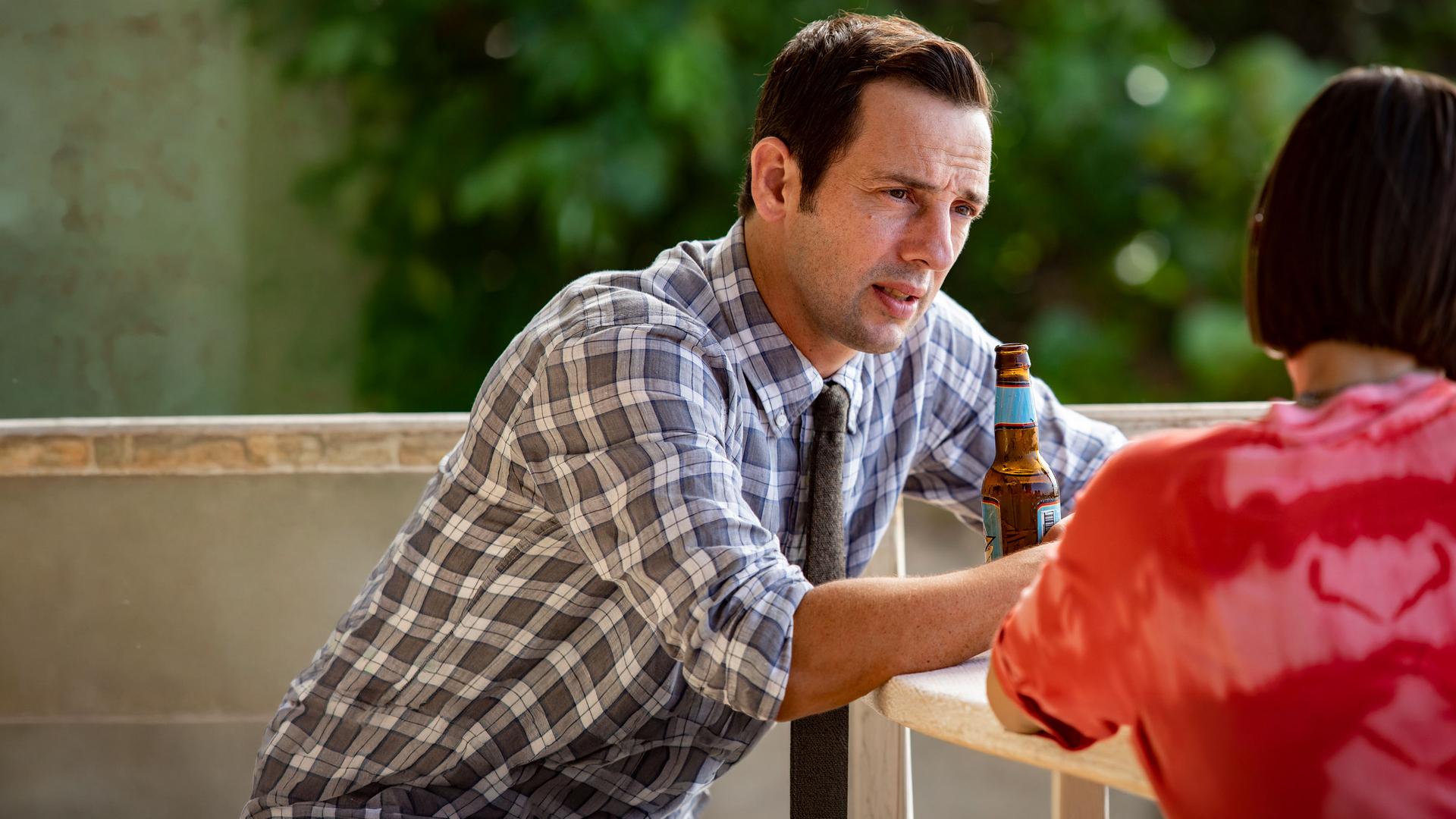 "Death in Paradise - Verwaschene Spuren": Neville (Ralf Little) sitzt mit Izzy (Kate O’Flynn) an einem Tisch und schaut sie verständnisvoll an.