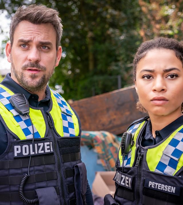 "Notruf Hafenkante - Verzweifelt": Großaufnahme des Polizisten Kris Freiberg (Marc Barthel) und dessen Kollegin Daisy Petersen (Aysha Joy Samuel). Sie stehen dicht nebeneinander und blicken in eine Richtung.