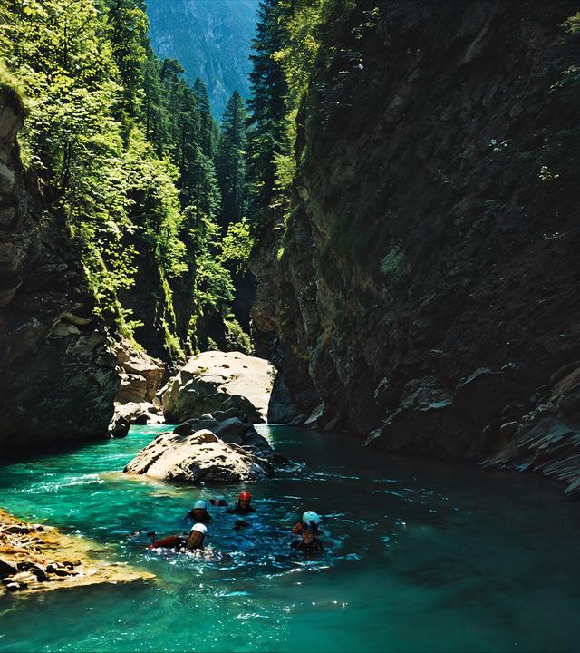 Eine Canyoning-Gruppe schwimmt durch die türkisfarbenen Gewässer der Viamala-Schlucht, umgeben von steilen, felsigen Klippen und üppiger Vegetation, ein lebendiges Beispiel für die Naturschönheiten der Schweiz.