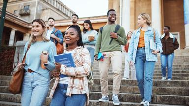 Mehrere Personen bewegen sich gemeinsam im Außenbereich eines Gebäudes eine Treppe hinunter, einige tragen Bücher und Unterlagen bei sich. Die Darstellung steht für ein diverses Miteinander in Bildung und Arbeitsumfeld.
