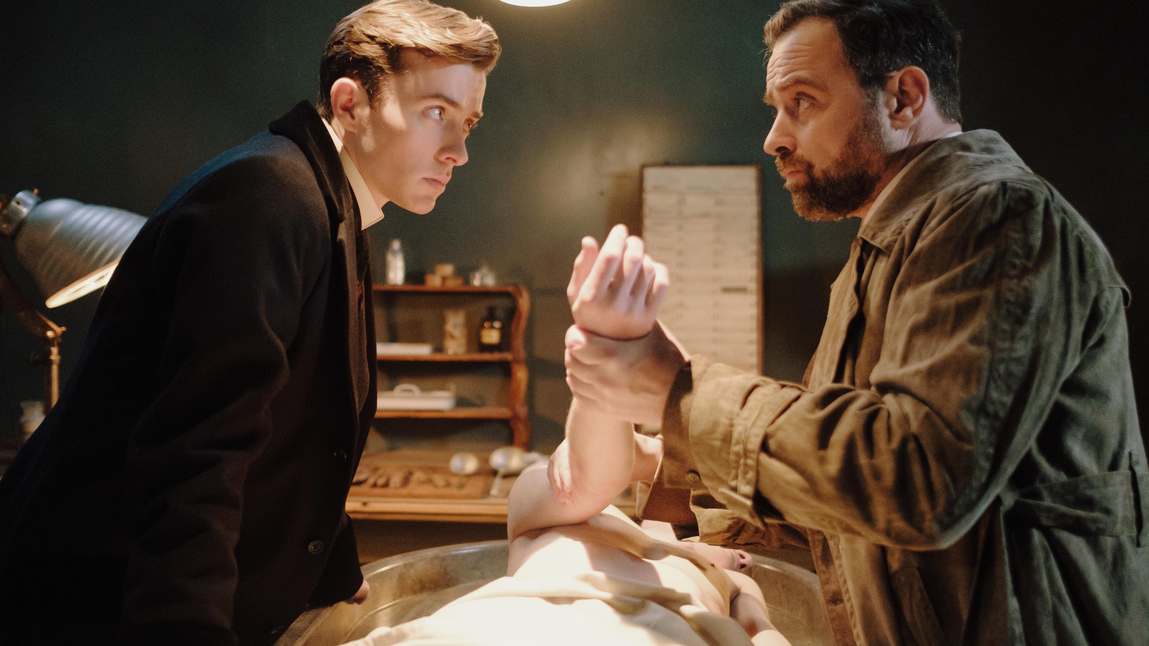 "Vienna Blood - Der verlorene Sohn": Max (Matthew Beard) und Oskar (Juergen Maurer) stehen vor einer Leiche, die mittig auf einem Tisch liegt.