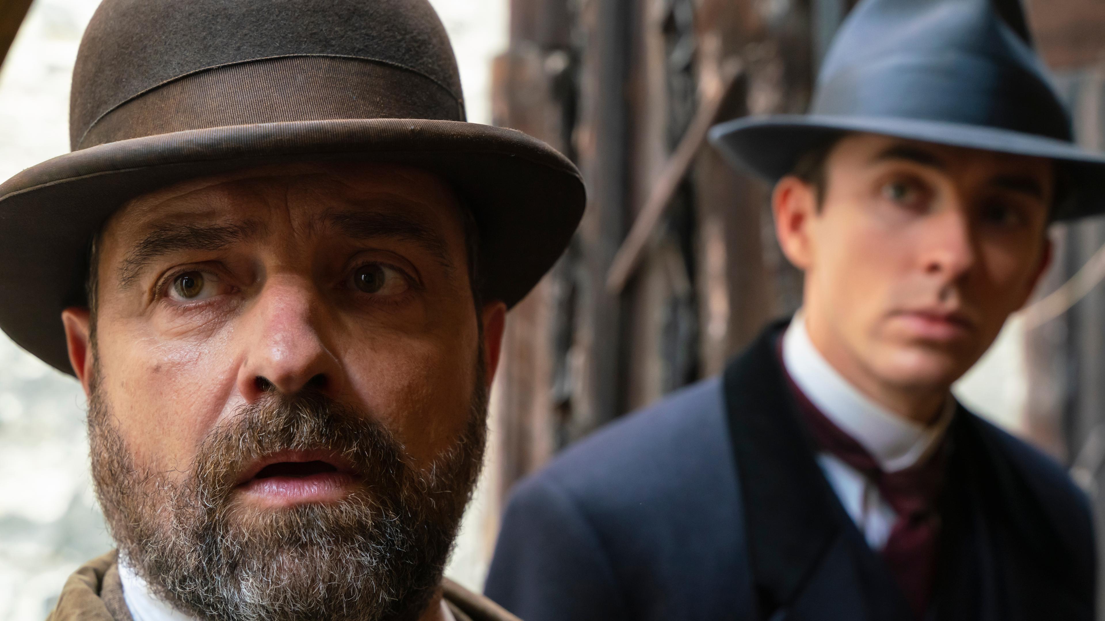 "Vienna Blood - Rendezvous mit dem Tod": Oskar Rheinhardt (Juergen Maurer) und im Hintergrund Max Liebermann (Matthew Beard) mit Hut bekleidet, stehen vor einem Gebäude.