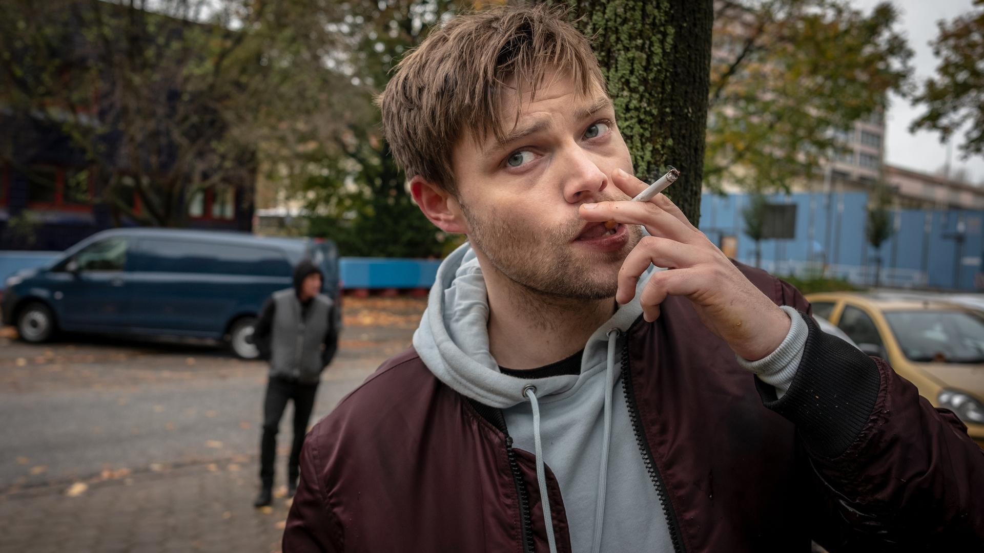 "Notruf Hafenkante - Vier Stunden Luft": Großaufnahme von Marvin Kessler (Julian Mau), der im Freien vor einem Baum steht und eine Zigarette raucht.