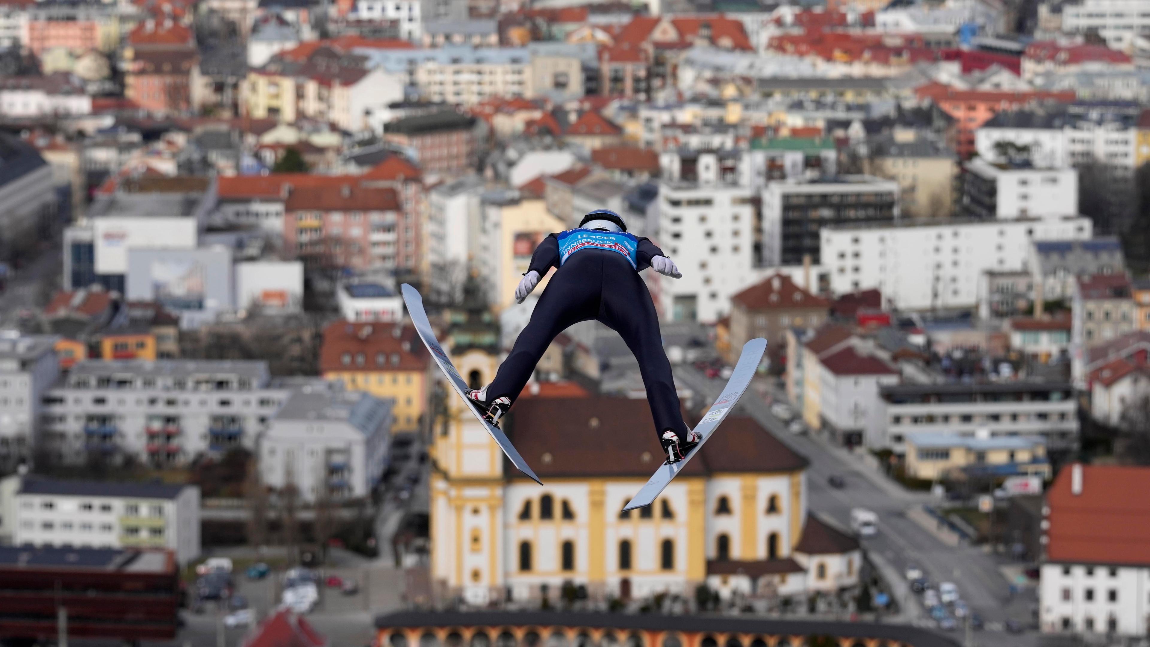 Ein Skipringer von hinten fliegt über eine Stadt